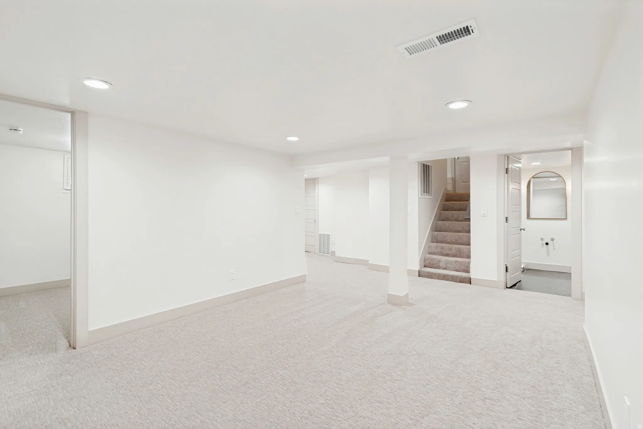 Spacious lower level featuring light-colored carpeting, recessed lighting, painted white walls, and a visible staircase with carpeted treads
