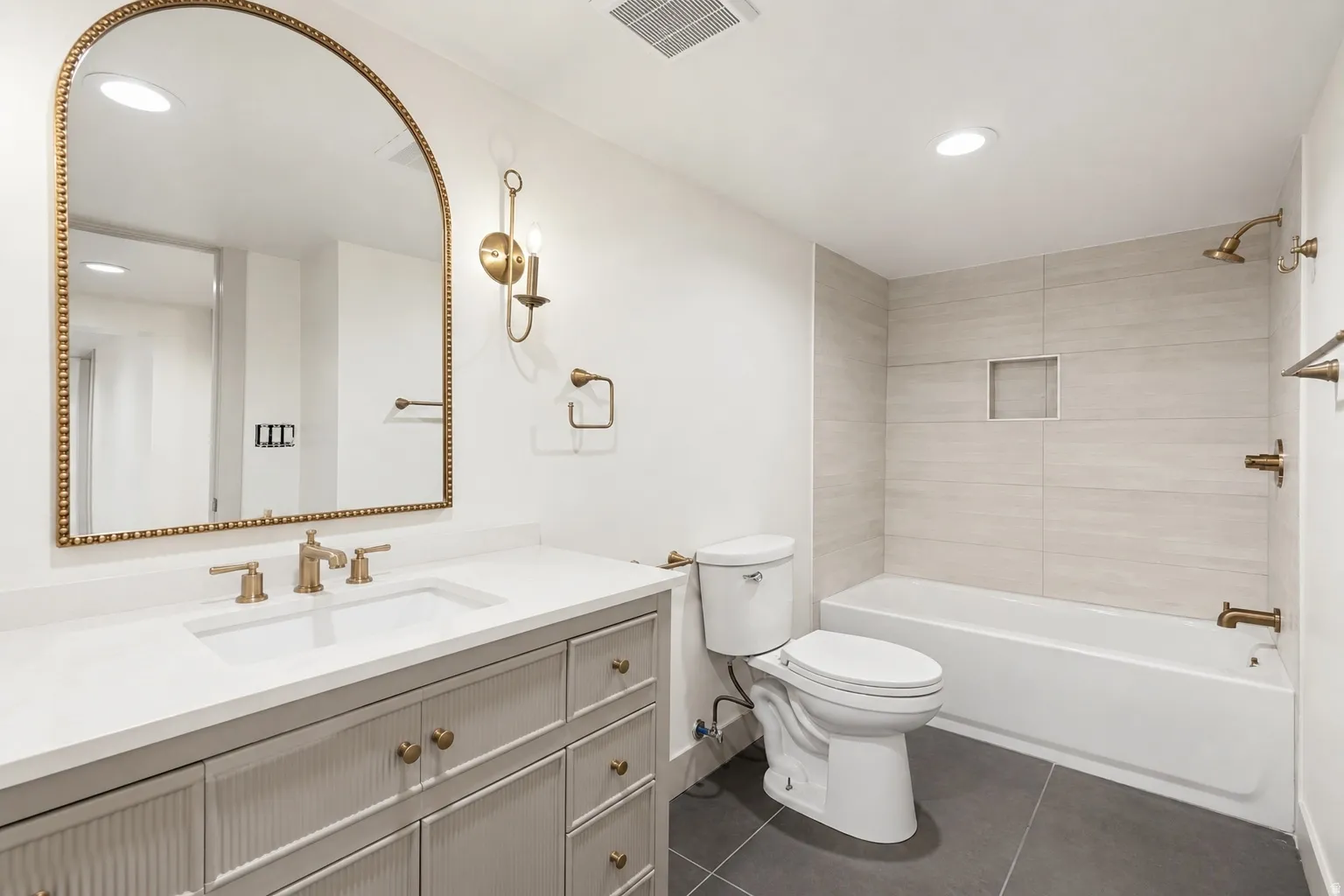 Bathroom featuring a single vanity with stone countertop, undermount sink, and brushed gold fixtures