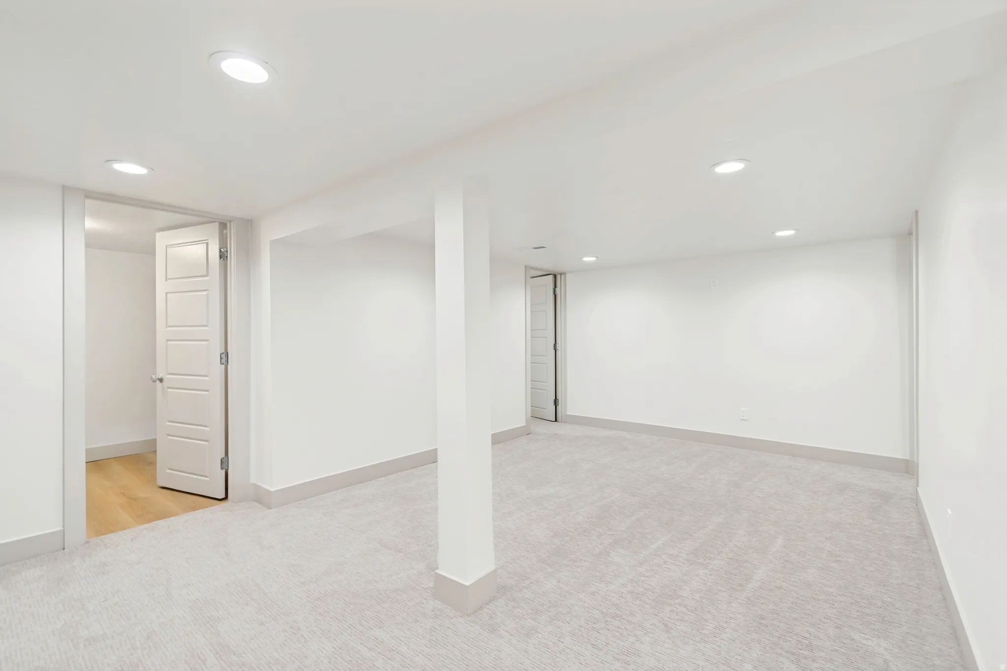 Spacious open room featuring recessed lighting, light-toned carpeting, and a white five-panel interior door