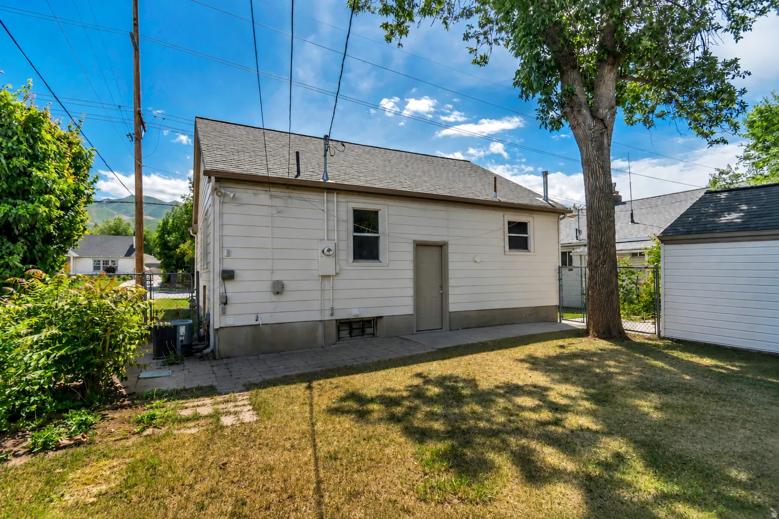 Spacious backyard featuring a large mature tree, a detached storage building, and a paved patio area