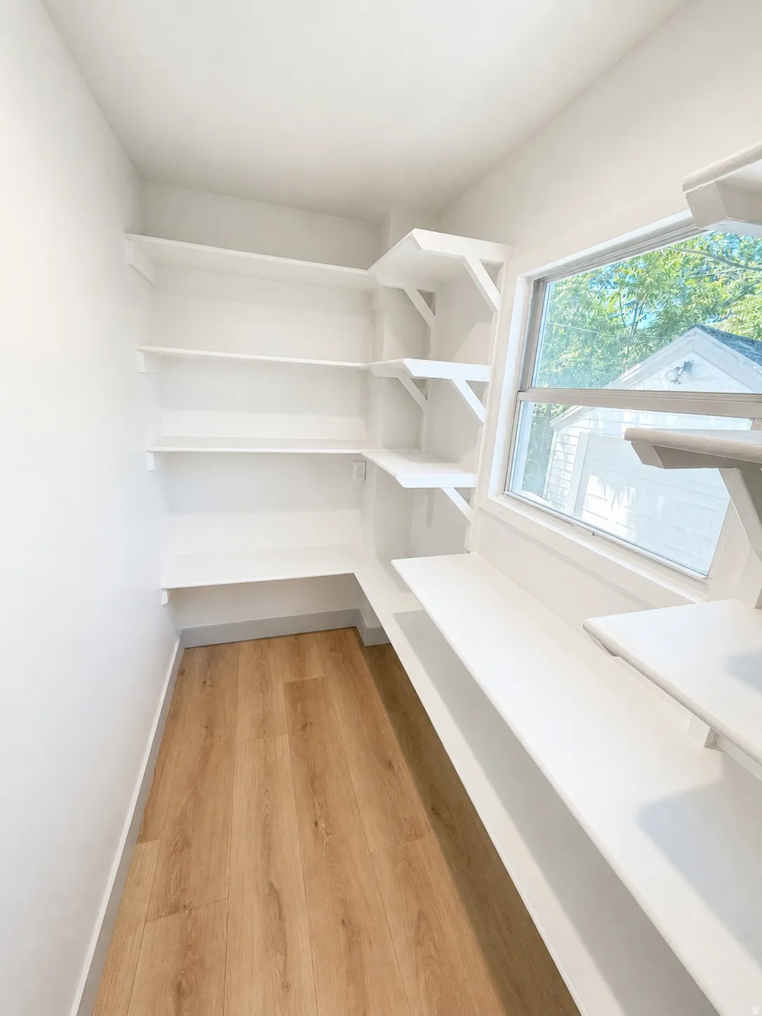 Corner pantry with white shelving, wood-finish flooring, and a single window
