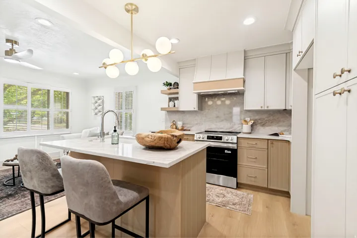 Modern kitchen featuring a central island with countertop seating, stainless steel appliances, a range hood with wood accents, and light wood-finish flooring