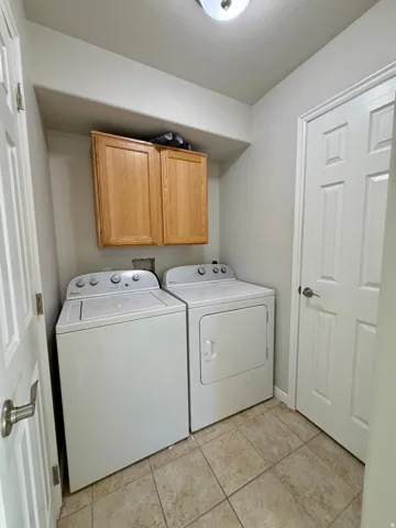 Dedicated laundry area featuring tile flooring, light-toned walls, and wood-finish cabinetry