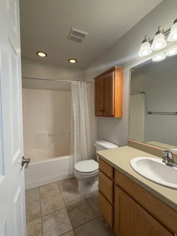 Full bathroom featuring a white bathtub with shower, toilet, and vanity with an integrated sink