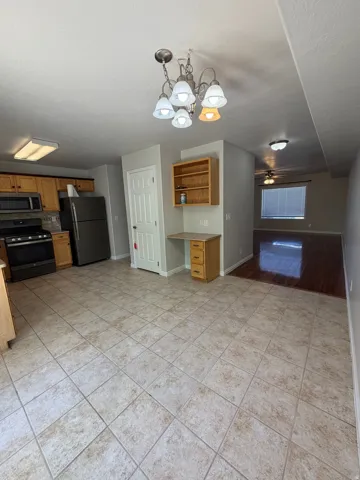 Kitchen area featuring tile flooring, wood-finish cabinetry, stainless steel appliances, and a built-in desk with shelving