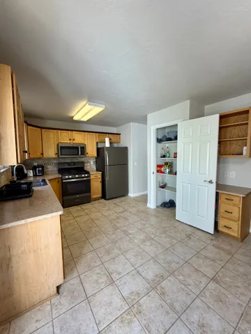 Kitchen featuring extensive cabinetry with wood-finish doors, durable tile flooring, a built-in pantry, and stone-look countertops