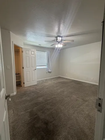 Carpeted interior room featuring a ceiling fan with light fixture, a window with blinds and curtain, and a closet with bifold doors and built-in shelving