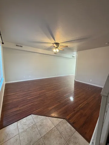 Spacious living area featuring polished wood-finish flooring, a ceiling fan with integrated lighting, and neutral wall tones