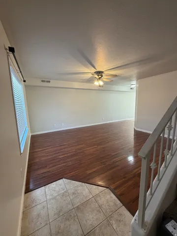 Open-concept living area featuring wood-finish flooring, a ceiling fan with integrated lighting, and a window with blinds