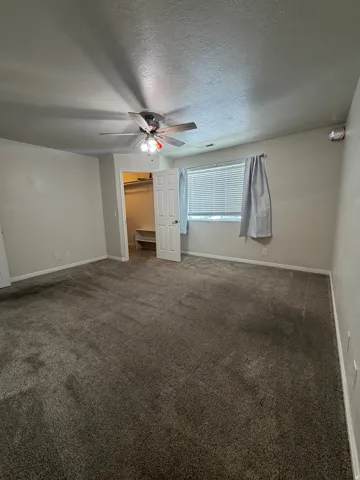 Spacious room featuring neutral carpeting, a ceiling fan with integrated lighting, and a window with blinds