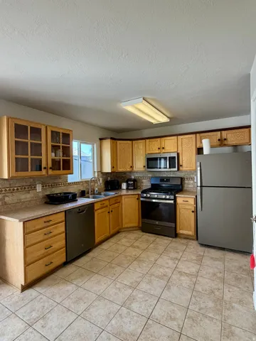 Kitchen featuring wood-finish cabinetry, stainless steel appliances, neutral tile flooring, and a patterned tile backsplash