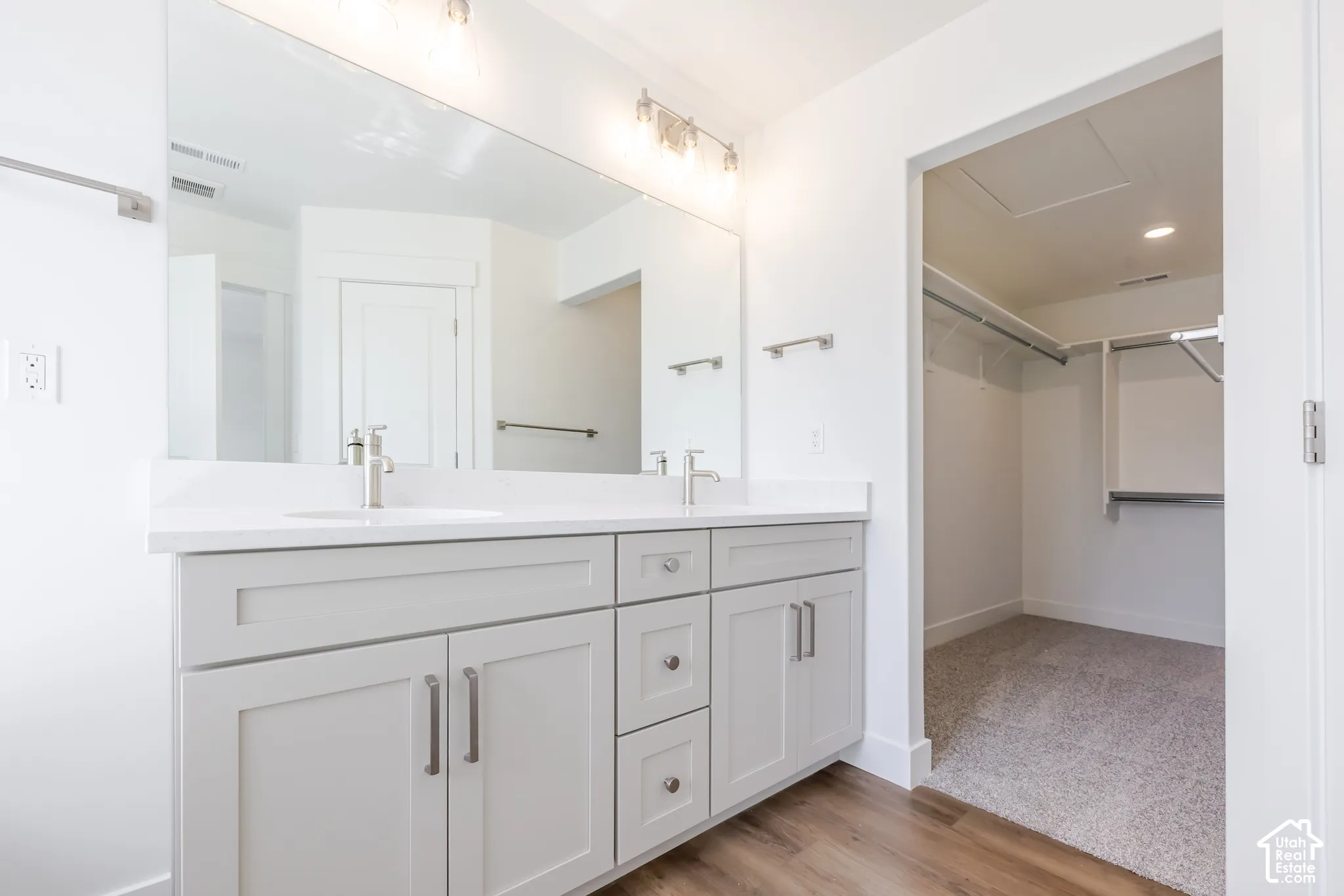 Dual vanity with white countertop, chrome fixtures, and light wood-finish flooring