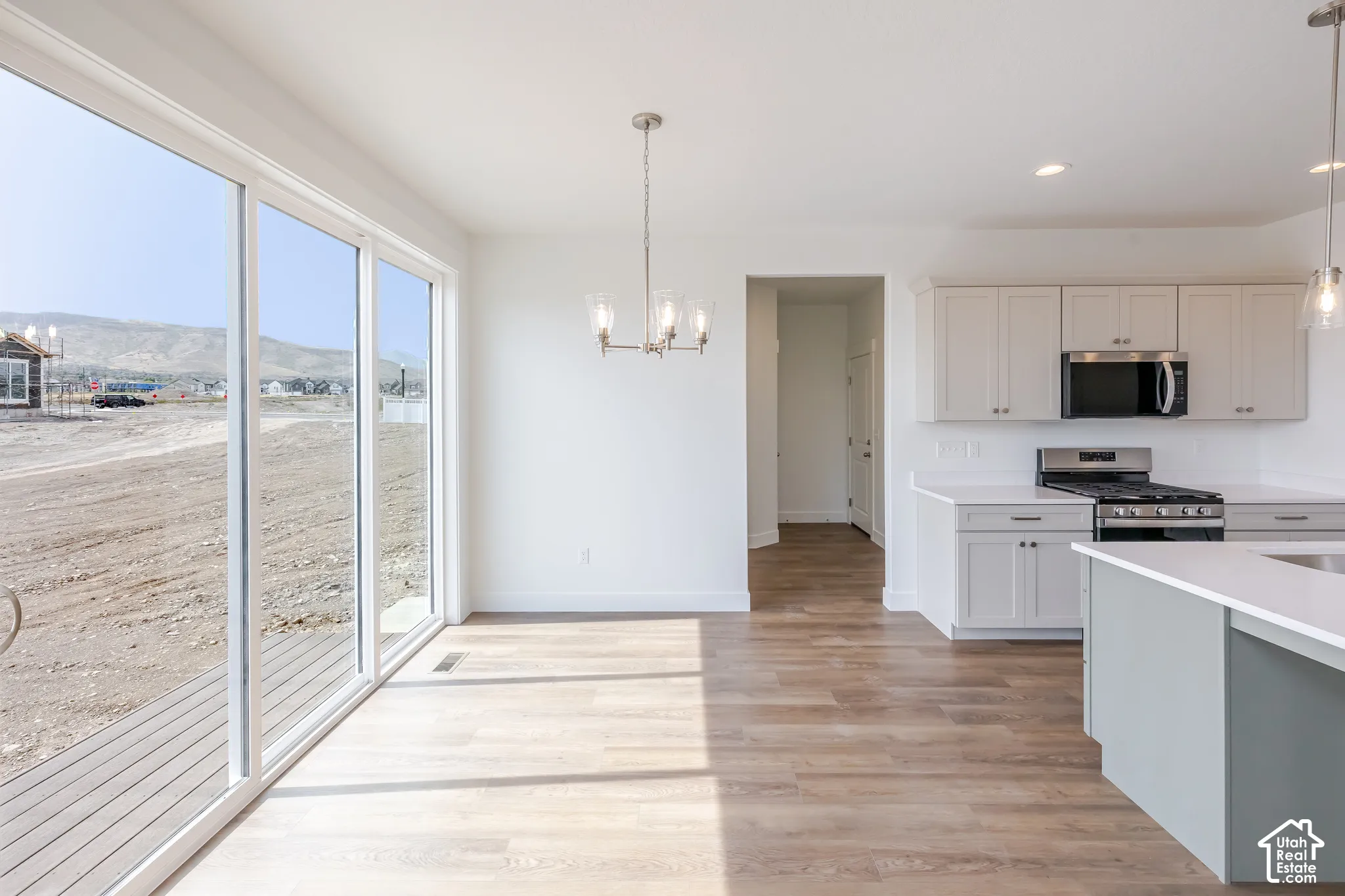 Open concept living space featuring wood-finish flooring, a contemporary chandelier, a kitchen with light-toned cabinetry, and stainless steel appliances