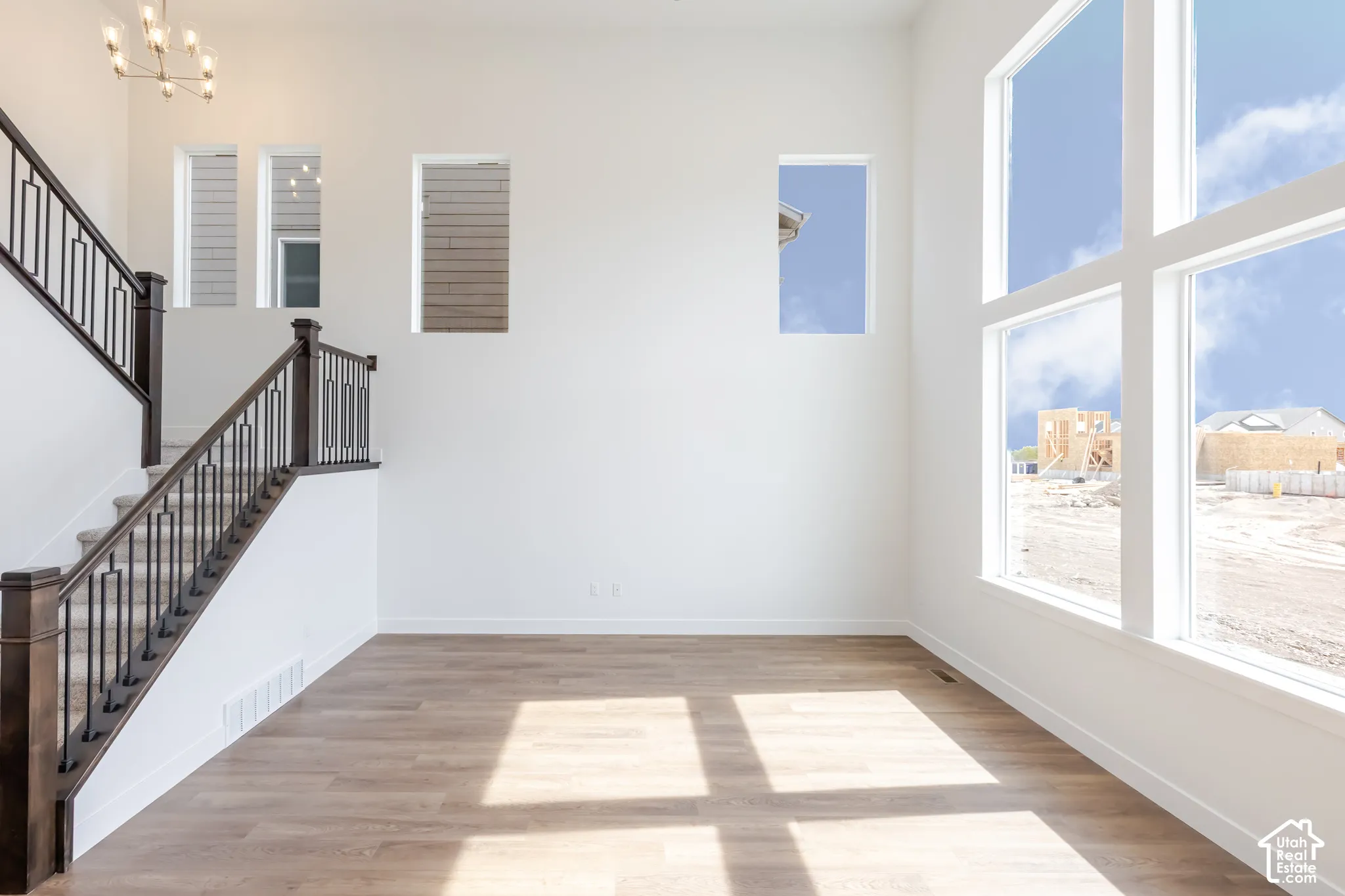 Wood-finish flooring, staircase with dark wood newel posts and metal balusters, high ceilings, large multi-pane windows, and a multi-arm chandelier