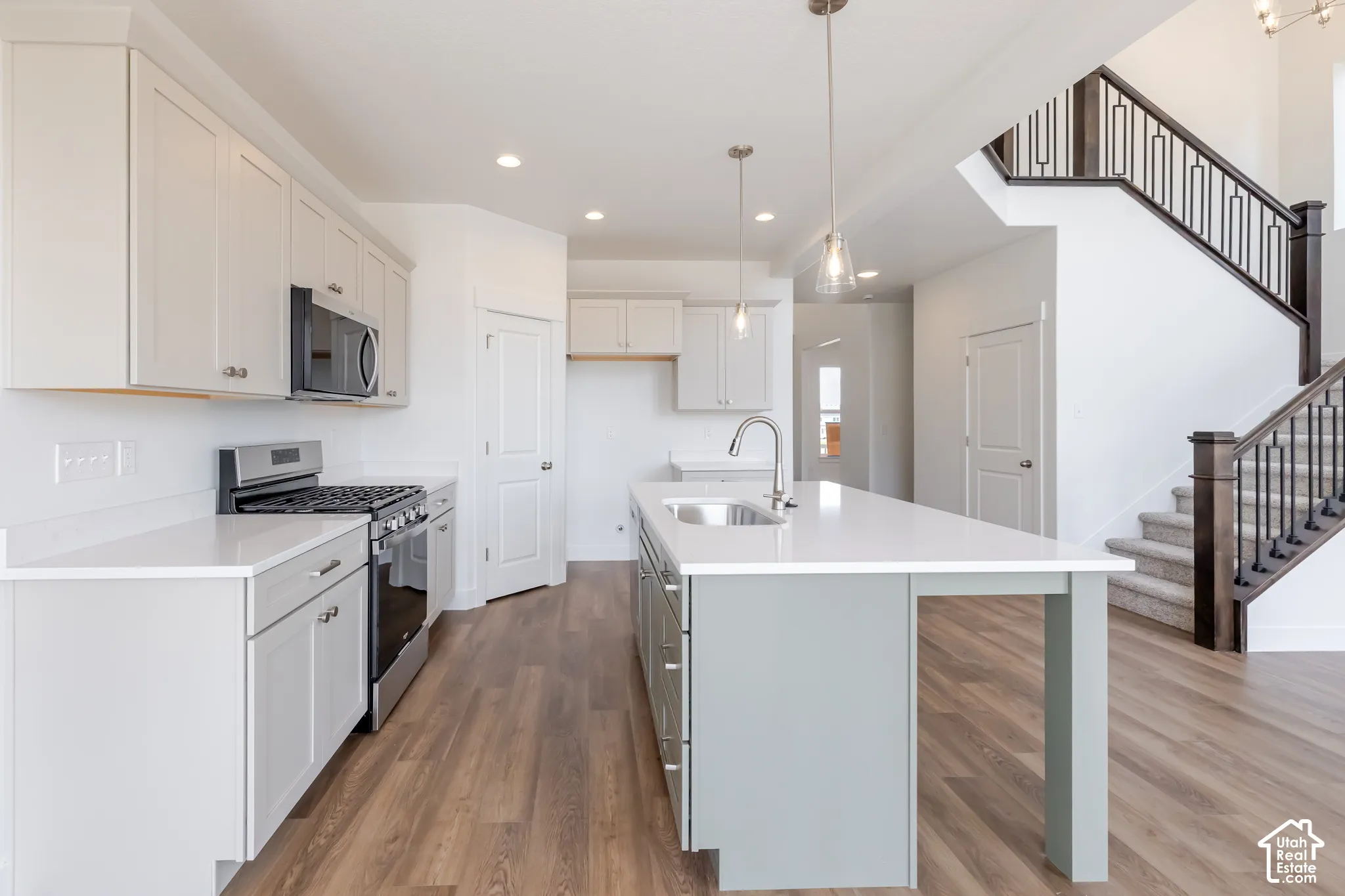 Kitchen featuring light-toned cabinetry, stainless steel appliances, a center island with a built-in sink, and pendant lighting