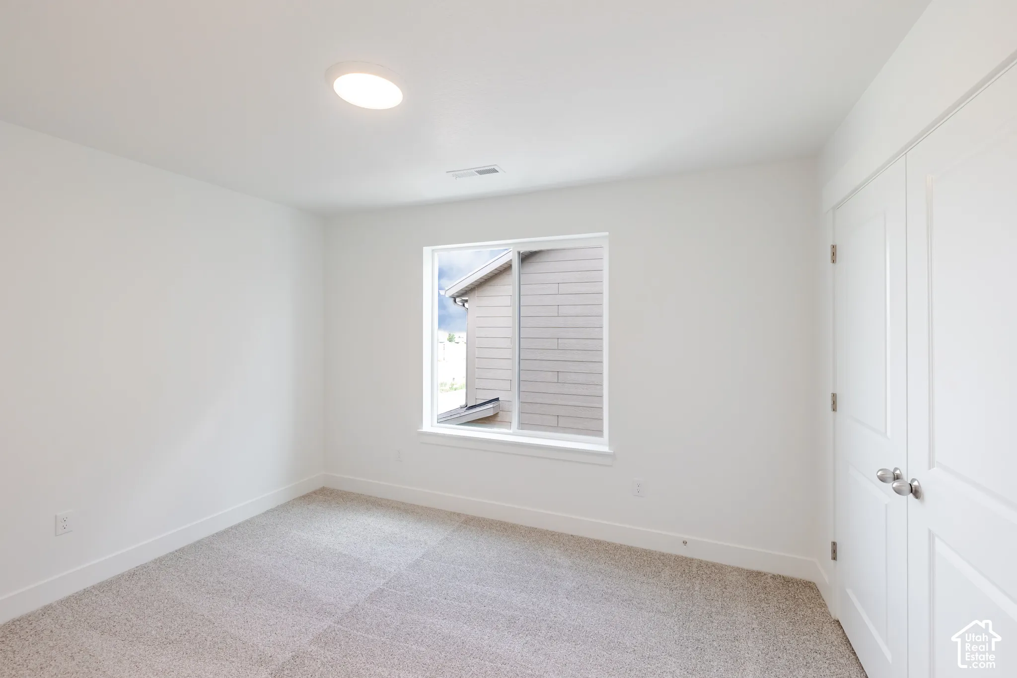 Recessed ceiling light, white walls, carpeted flooring, window with white trim, and white bi-fold doors