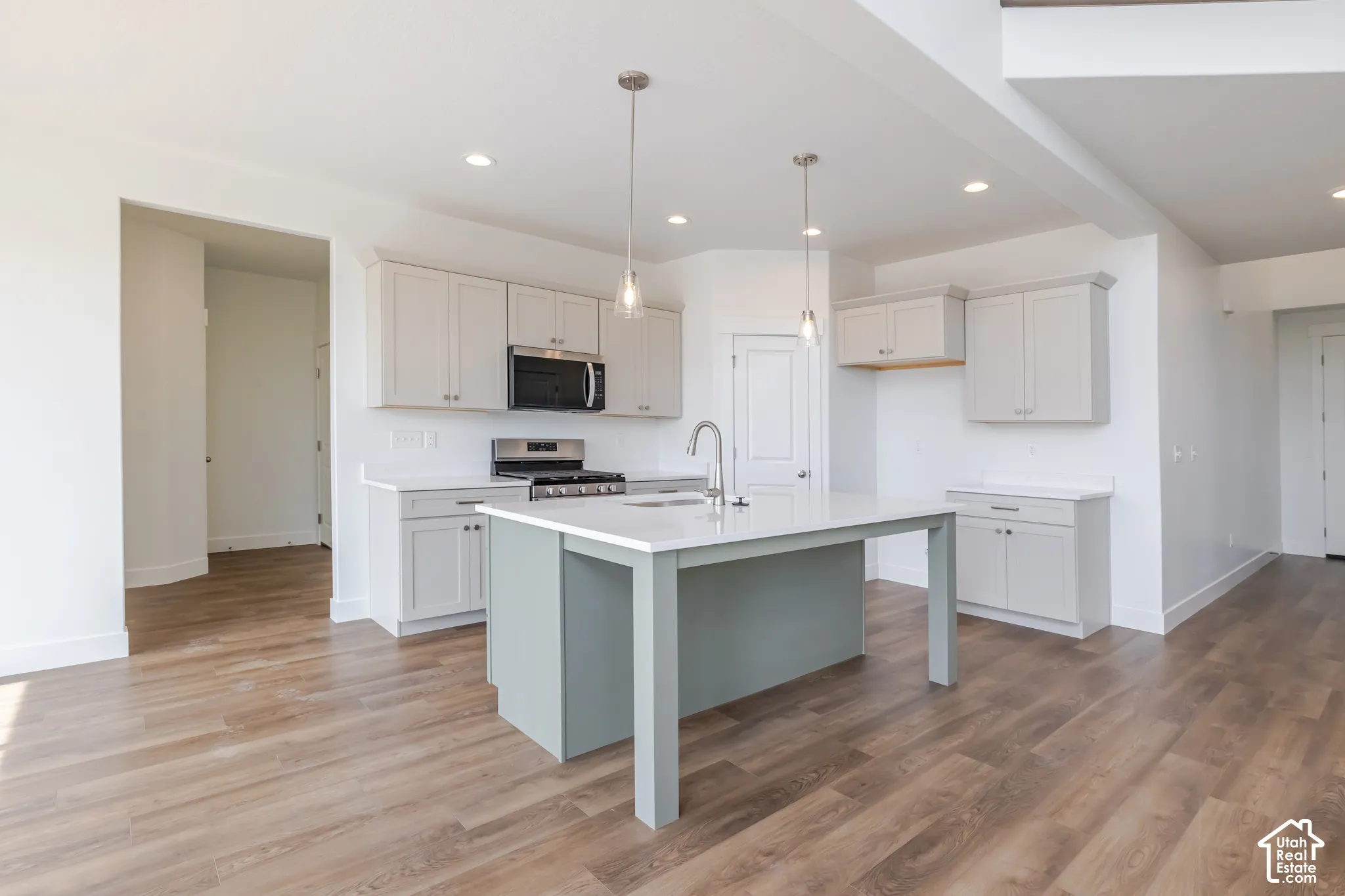 Kitchen featuring a central island, light-toned cabinetry, stainless steel appliances, and wood-finish flooring