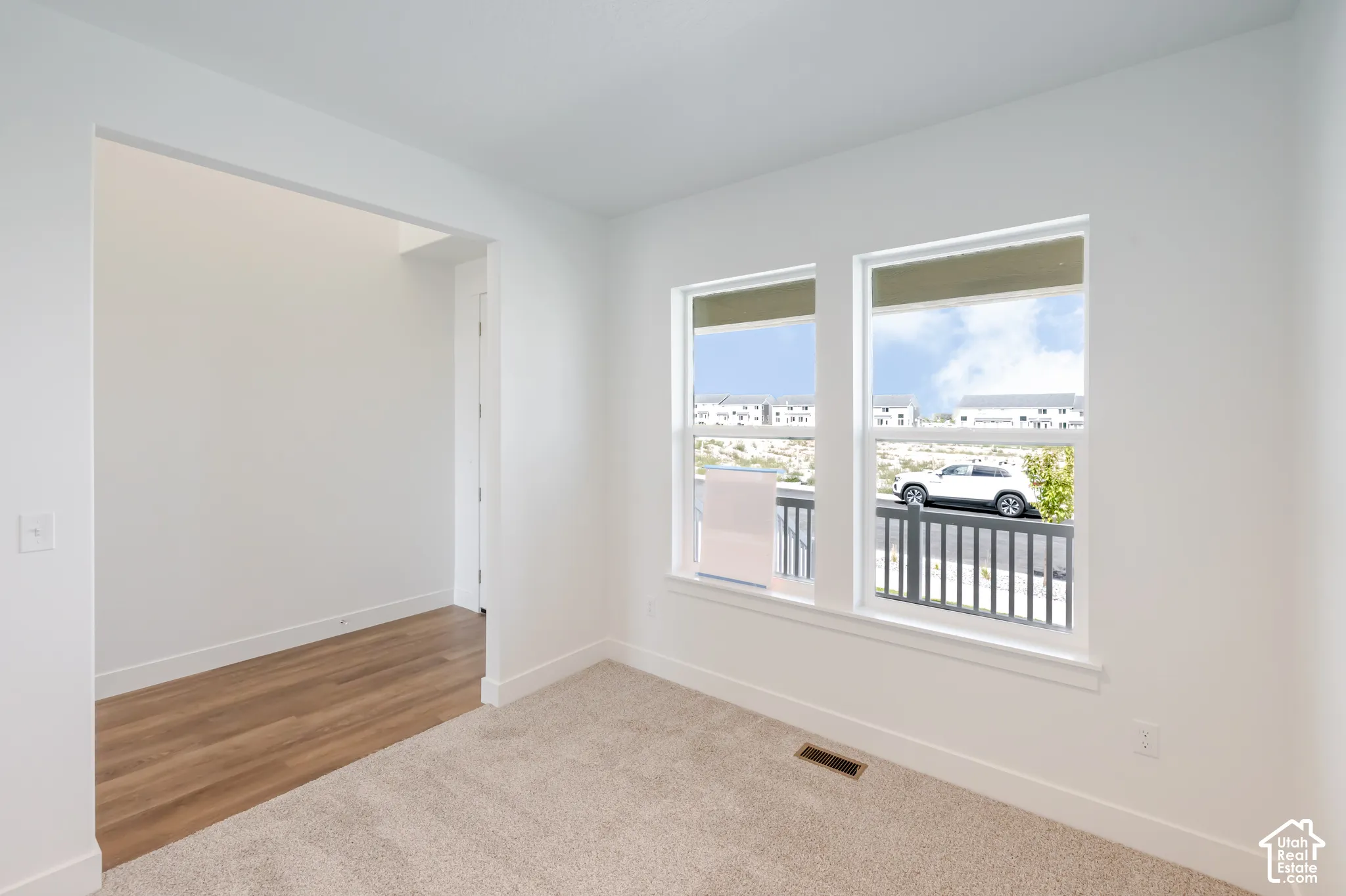Dual windows, neutral-tone carpeting, wood-finish flooring, and white trim