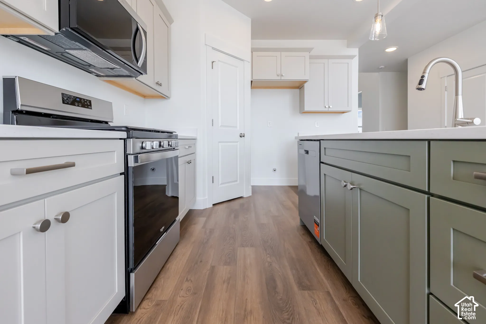 Kitchen featuring stainless steel appliances, wood-finish flooring, white shaker cabinets, an island with sage green shaker cabinets, and a gooseneck faucet