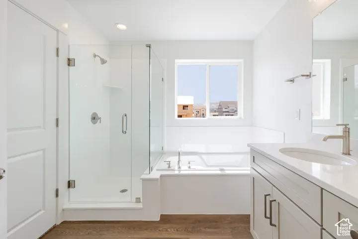 Spacious bathroom featuring a glass-enclosed shower, built-in bathtub, dual-pane window, single vanity with an integrated sink, and wood-finish flooring