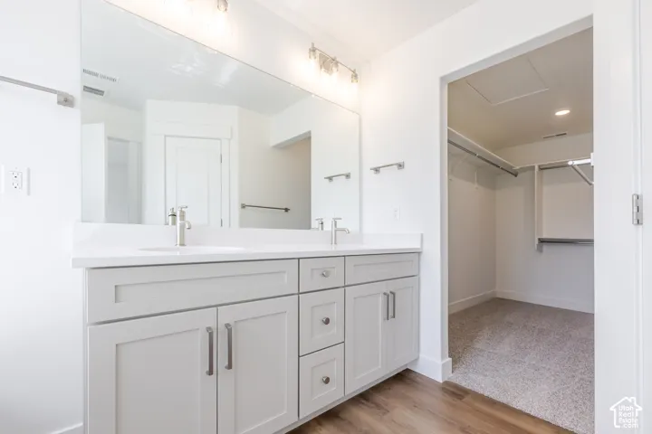 Dual vanity with white countertop, chrome fixtures, and light wood-finish flooring