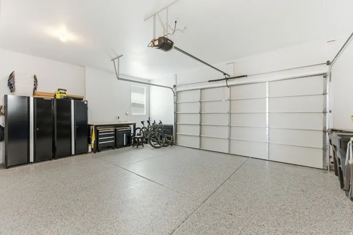 Spacious garage featuring a light-toned epoxy floor, an automatic overhead garage door, a window with horizontal blinds, and overhead lighting