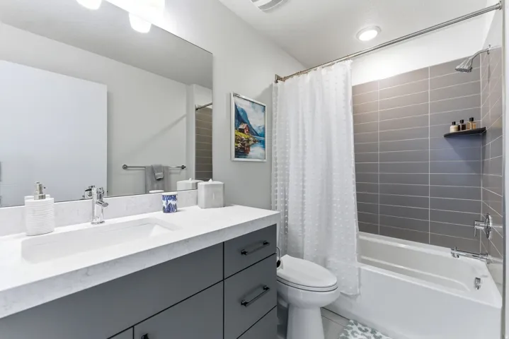 Bathroom featuring a single vanity with a white countertop, an undermount sink, and gray cabinetry with black hardware