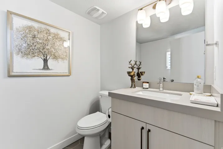 Bathroom featuring a light wood-finish vanity with a single basin sink, a gray countertop, and an overhead vanity light fixture