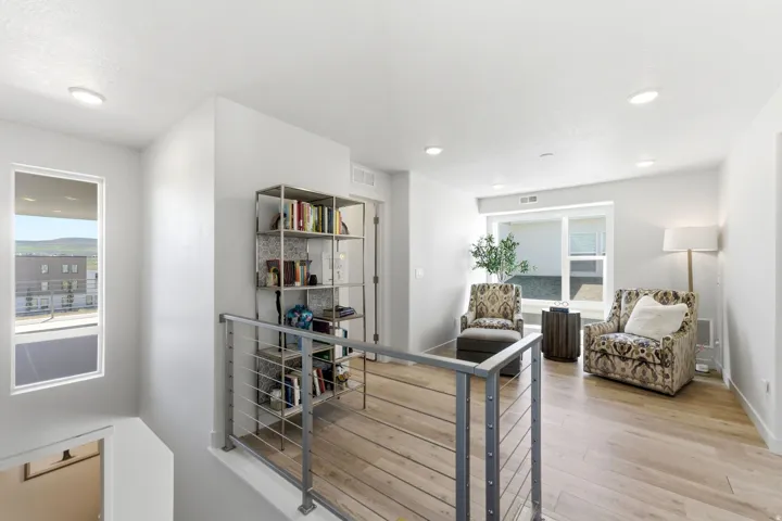 Upper-level landing featuring light wood-finish flooring, recessed lighting, and a contemporary metal railing