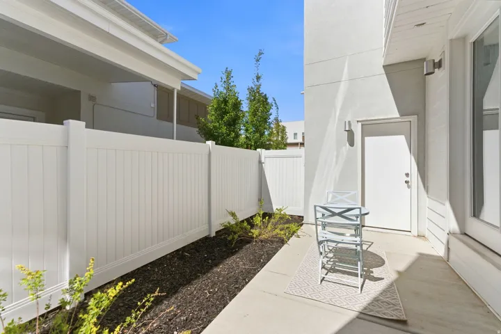 Private outdoor patio space featuring a concrete slab, white privacy fencing, exterior door access, and wall-mounted lighting fixtures