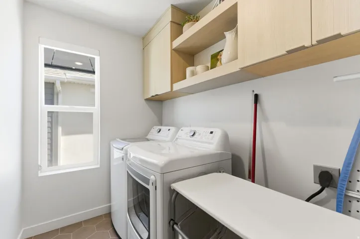 Utility room with a window, hexagon tile flooring, and light wood-finish cabinetry