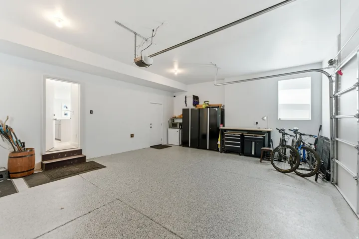Garage featuring a speckled epoxy floor, white painted walls, overhead lighting, and a roll-up garage door with tracks