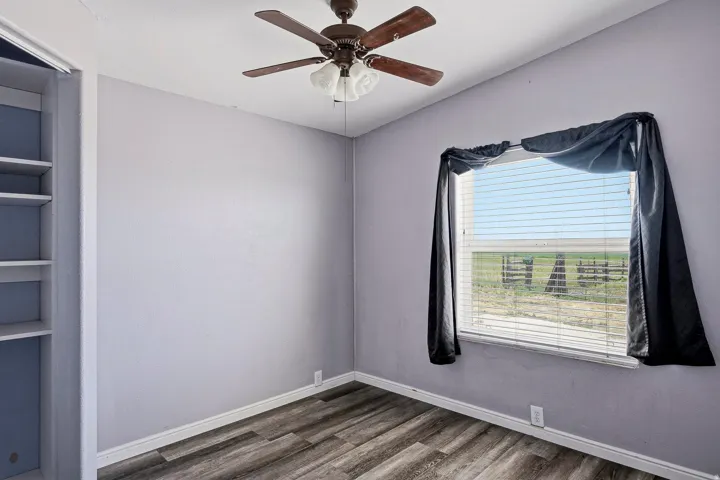 Interior room featuring wood-finish flooring, a ceiling fan with integrated lighting, built-in shelving, and a window with horizontal blinds