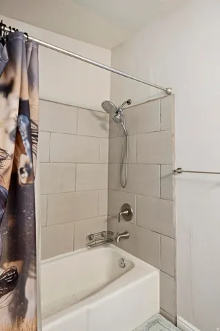 White bathtub with a tiled surround, brushed nickel fixtures, and a multi-setting showerhead