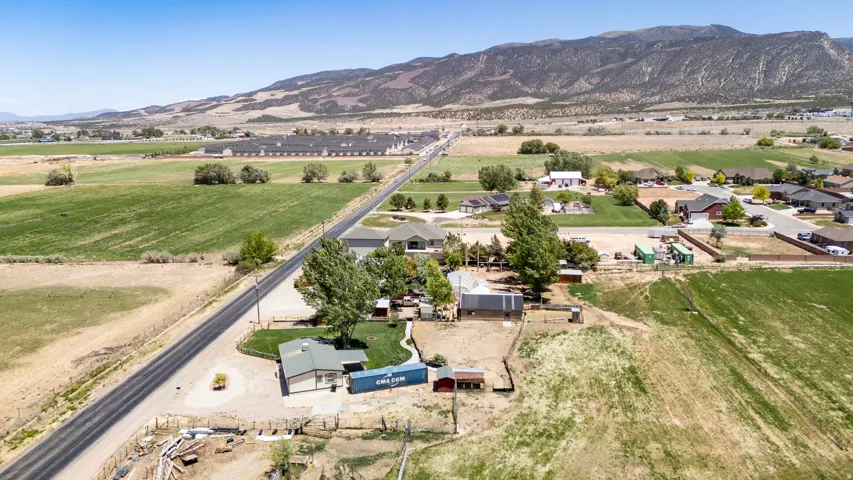 Expansive property featuring a residence with a green roof, a paved road spanning the property, surrounding agricultural fields, and distant mountains