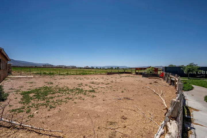 Expansive outdoor space featuring a rustic wood fence, a large open field, a small shed structure, and a paved pathway