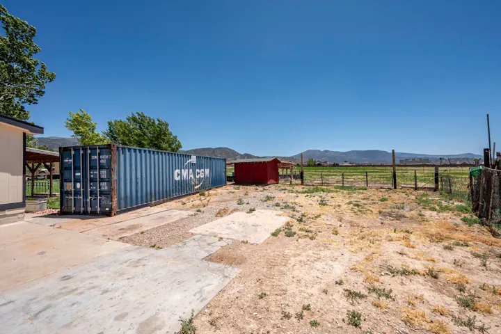 Expansive outdoor space featuring a blue shipping container, a red shed, and a fenced perimeter
