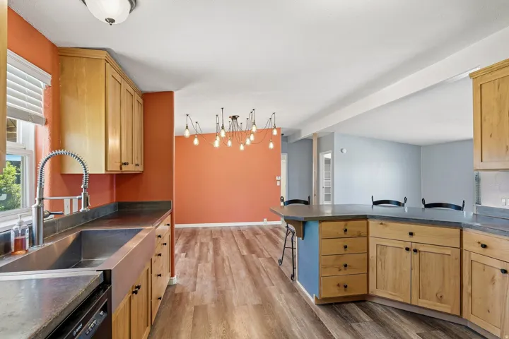 Kitchen featuring wood cabinetry, a stainless steel farmhouse sink, a gooseneck pull-down faucet, and dark countertops