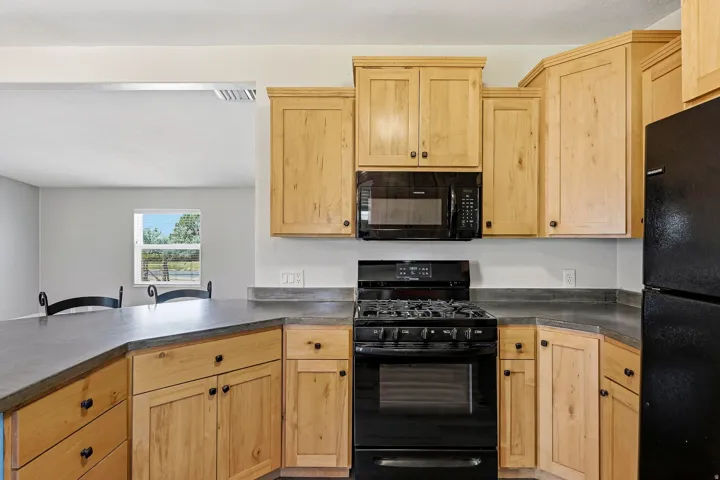 Kitchen featuring wood cabinetry, dark countertops, and black appliances