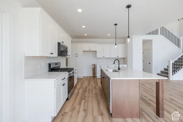 Kitchen featuring white cabinetry, light-toned wood-finish flooring, a central island with a sink, and stainless steel appliances