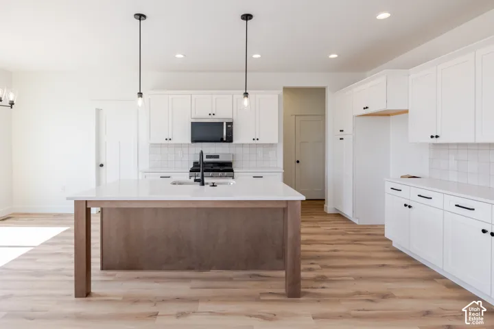 Kitchen featuring white cabinetry, a wood-finish island, light-toned wood-finish flooring, white subway tile backsplash, and stainless steel appliances