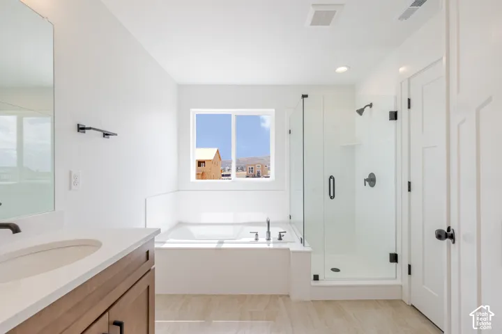 Light-filled bathroom featuring a built-in soaking tub, walk-in shower with clear glass enclosure, wood-finish vanity with countertop, and modern matte black fixtures