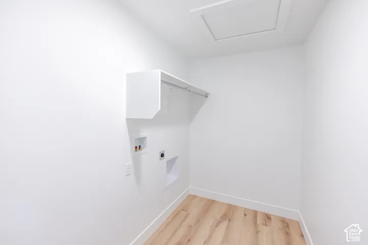 Dedicated laundry area featuring wood-finish flooring, white walls, and an overhead storage shelf with a clothing rod