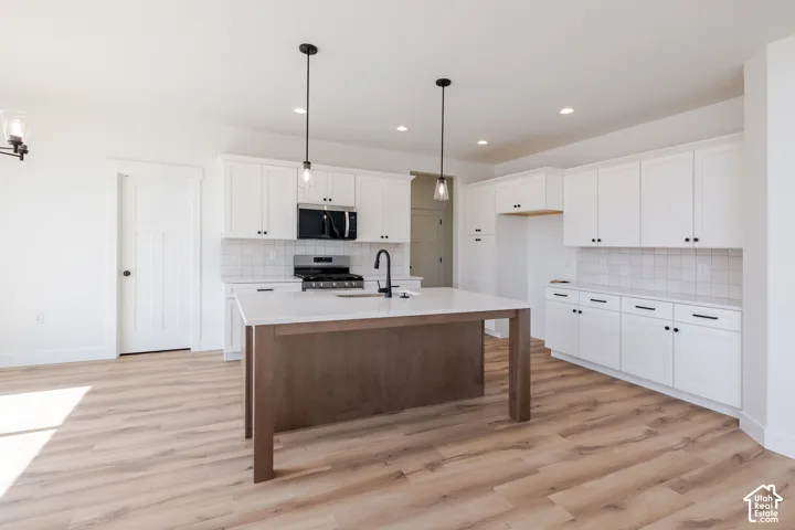 Expansive kitchen featuring wood-finish flooring, white cabinetry, a large center island with a light-toned countertop, a tile backsplash, and recessed lighting