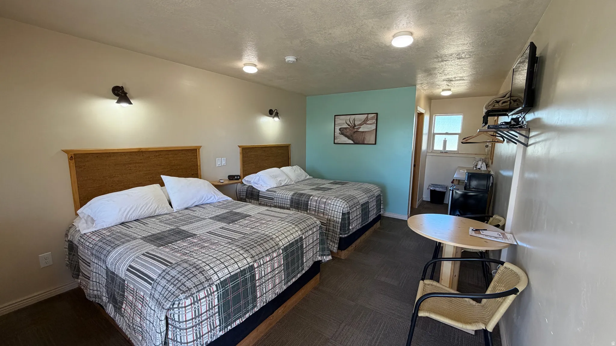 Room featuring two beds with wood-finish headboards, wall-mounted lighting, and a mounted flat-screen television