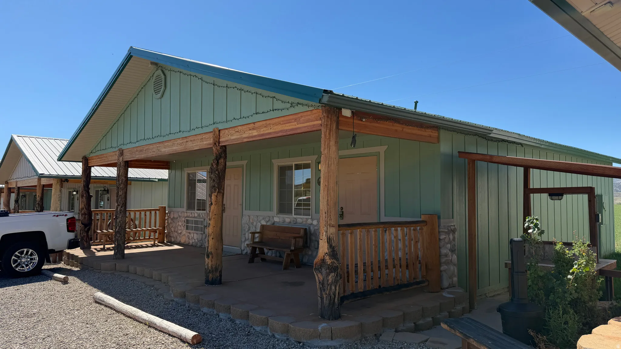 Exterior facade featuring a covered porch with natural wood posts, stone accents, and a light green siding finish
