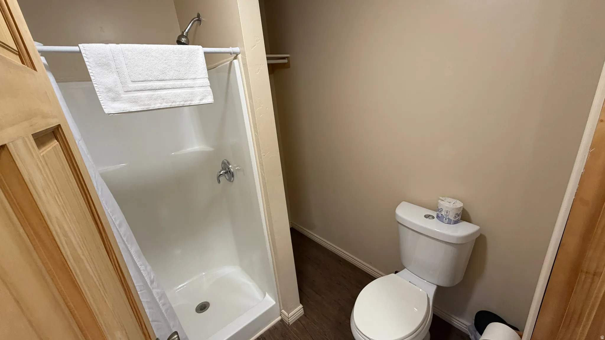 Bathroom featuring a white shower stall with chrome fixtures, a white toilet, wood-finish flooring, and light-toned wall paint