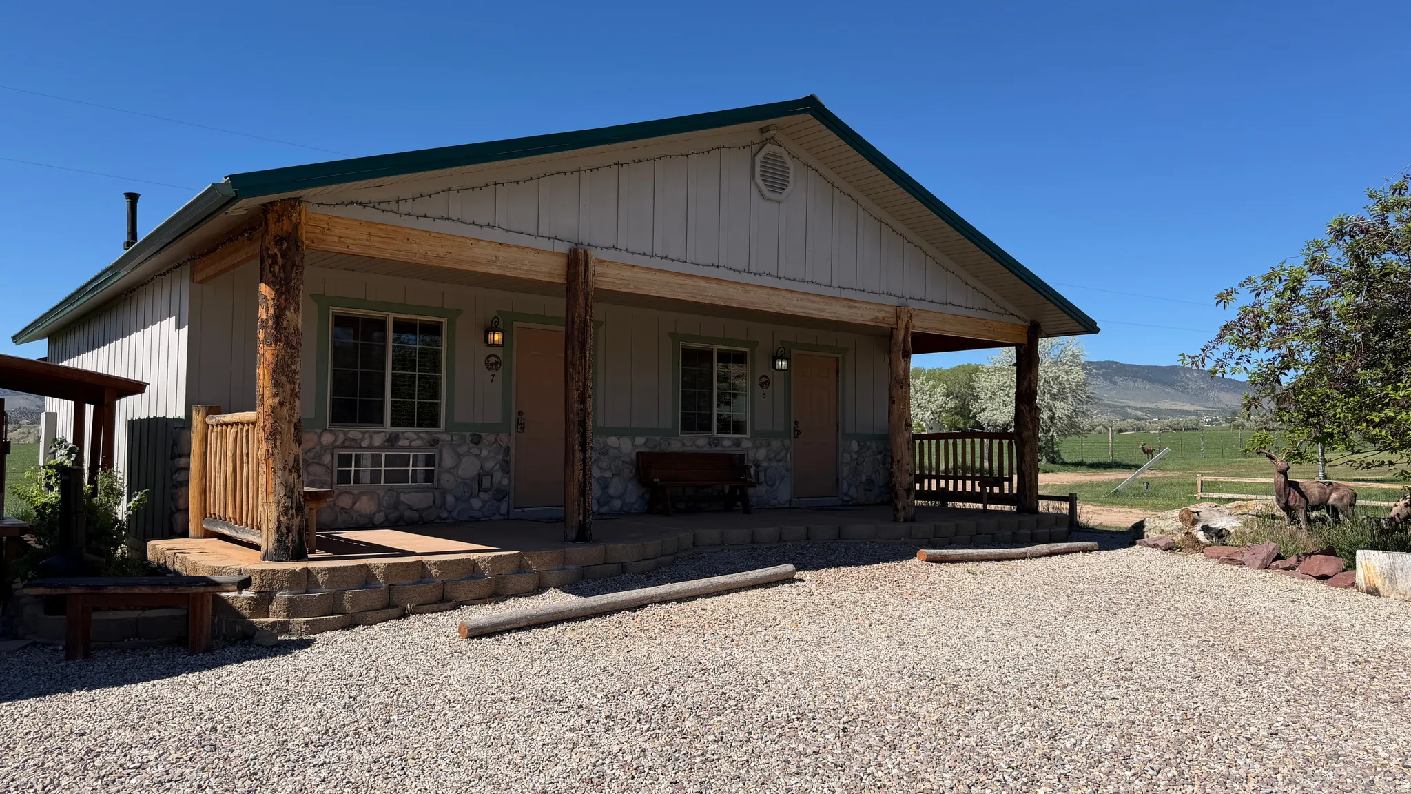Two-unit structure with natural wood posts and railing, stone veneer facade, and a gravel parking area