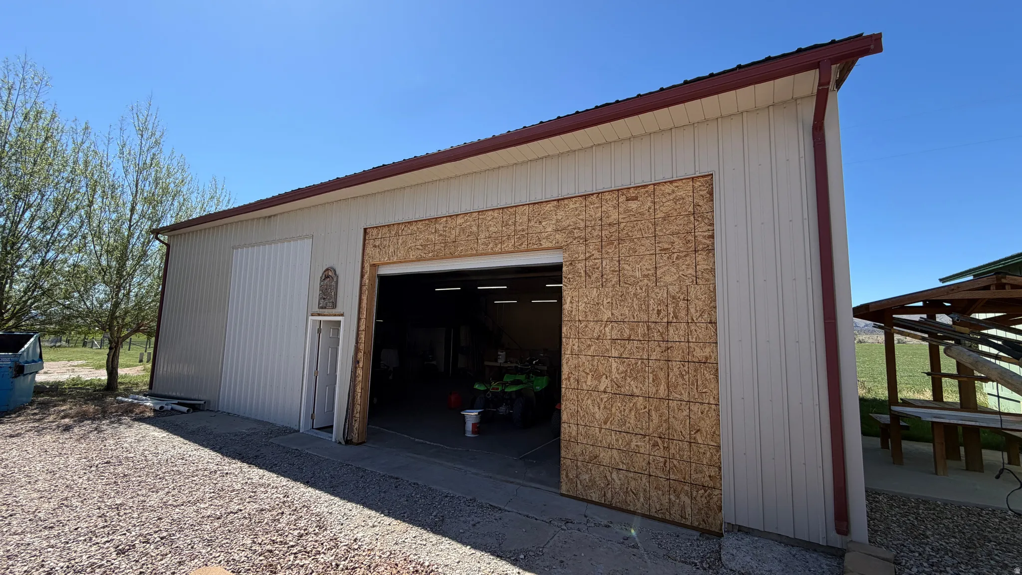 Metal-sided outbuilding featuring a sloped roof with gutters, a large garage door opening, and a side access door