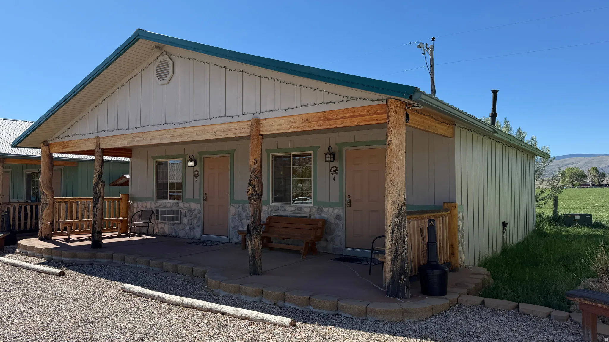 Exterior featuring a covered porch with rustic wood posts, a green metal roof, light-colored siding, and stone veneer accents